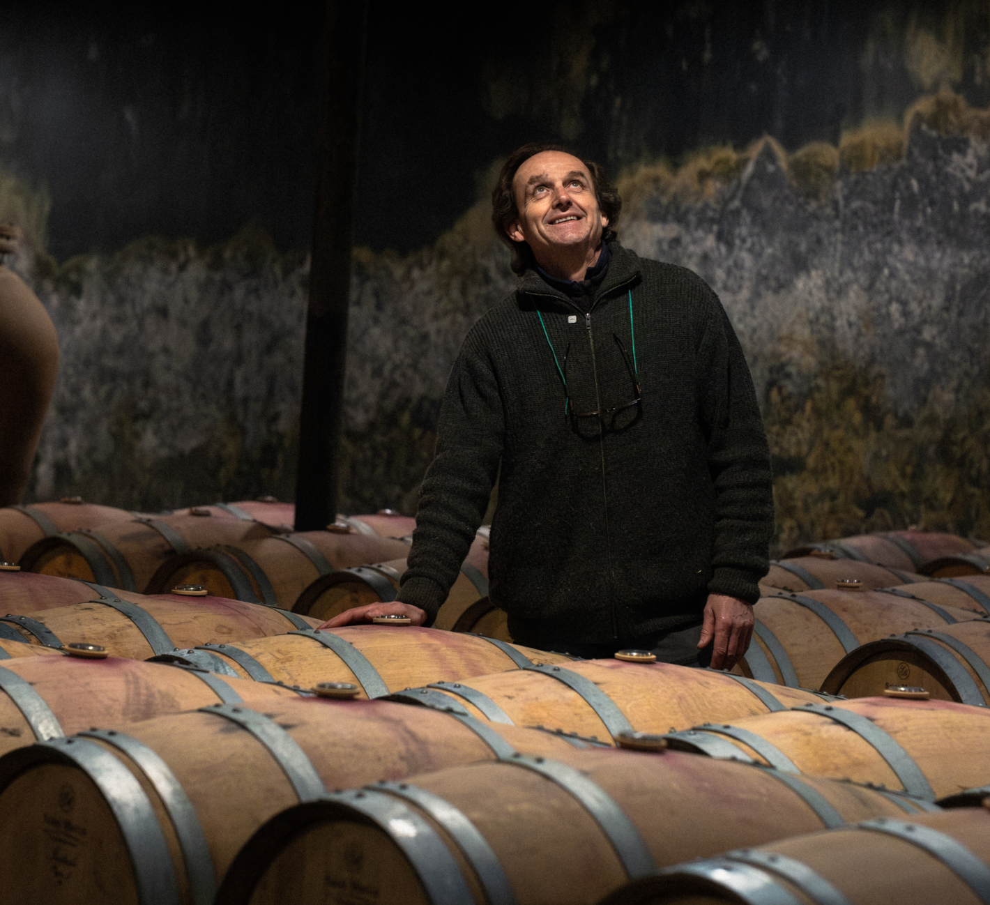 Notre histoire, notre terroir – Maison Sichel Homme souriant dans un chai entouré de barriques, notre histoire notre terroir
